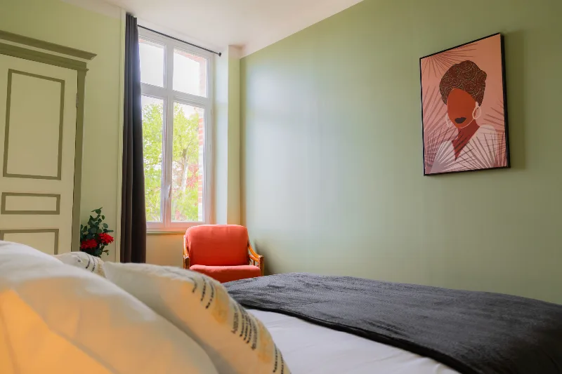 Chambre avec lit double, linge blanc et noir, armoire ancienne et fauteuil en rotin orange