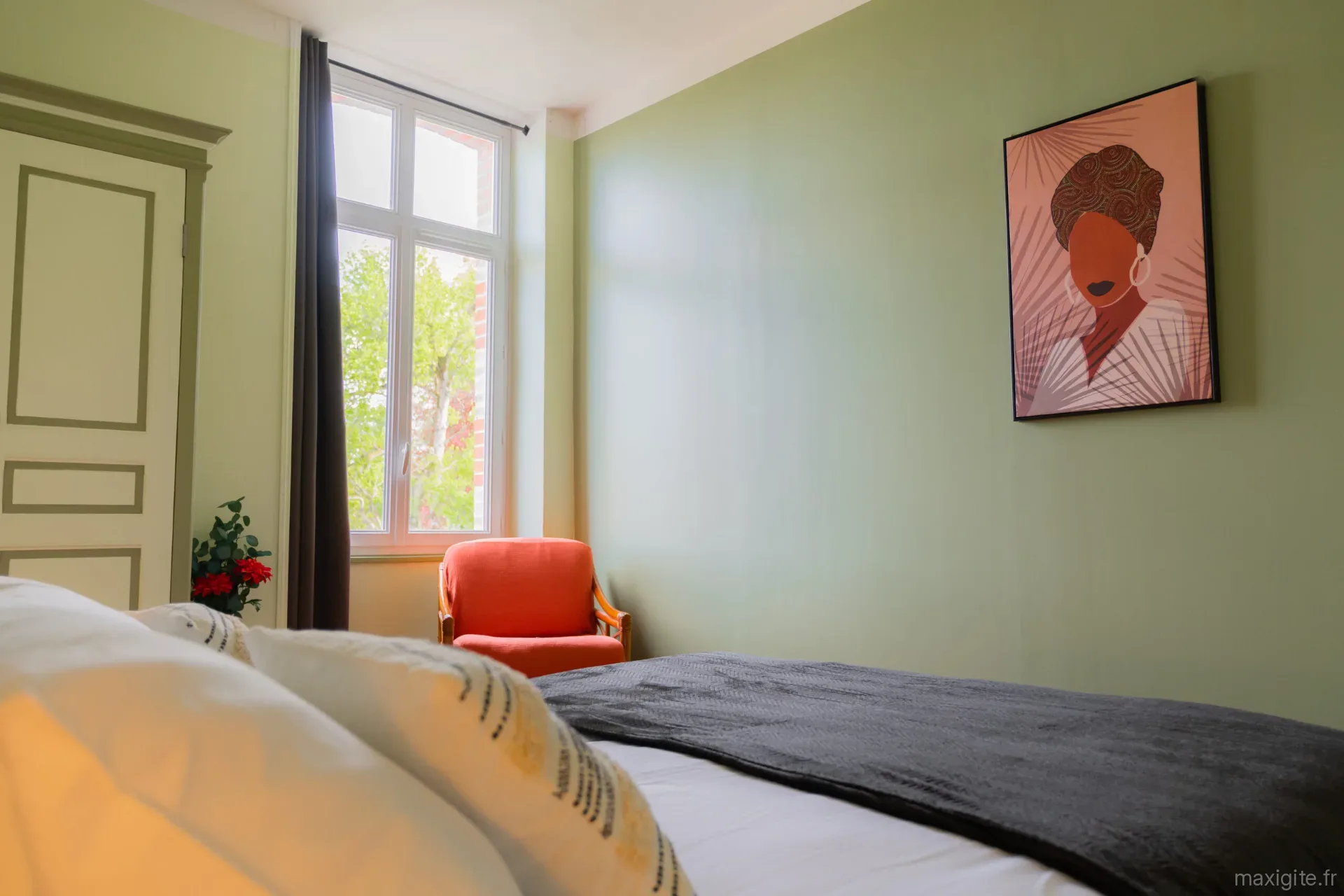 Chambre avec lit double, linge blanc et noir, armoire ancienne et fauteuil en rotin orange