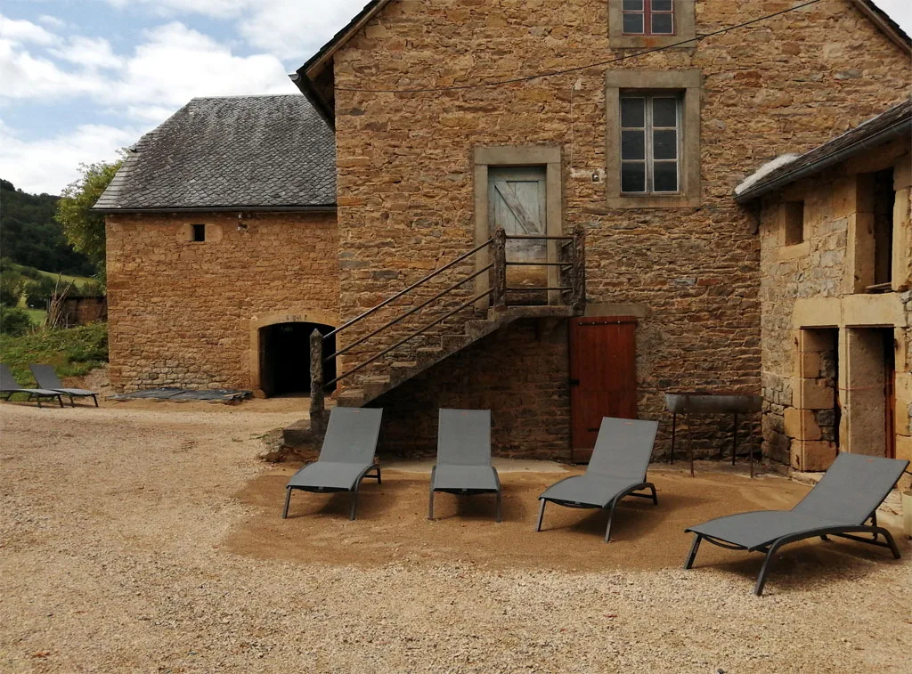 Terrasse extérieure avec quatre chaises longues face à la bâtisse en pierre du pays