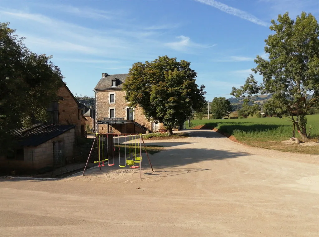 Chemin d'accès gravillonné avec aire de jeux pour enfants devant la bâtisse en pierre