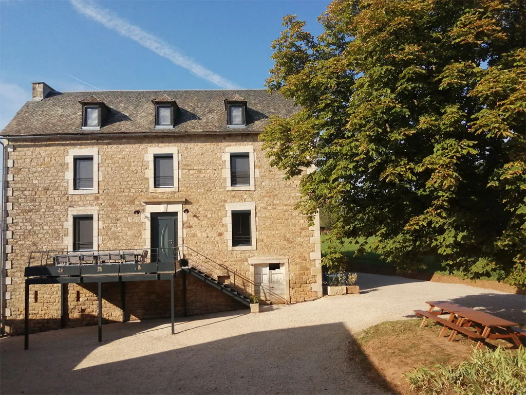 Façade arrière en pierre avec grande terrasse en bois surélevée et mobilier de jardin