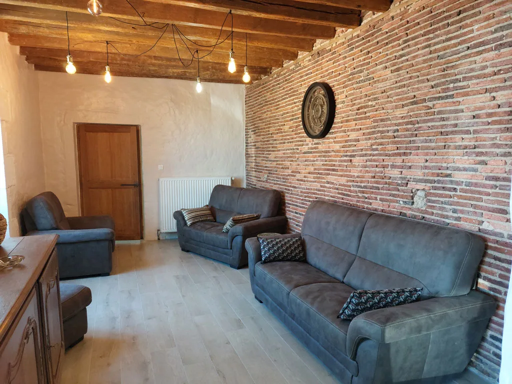 Salon chaleureux avec canapés gris et mur en briques apparentes