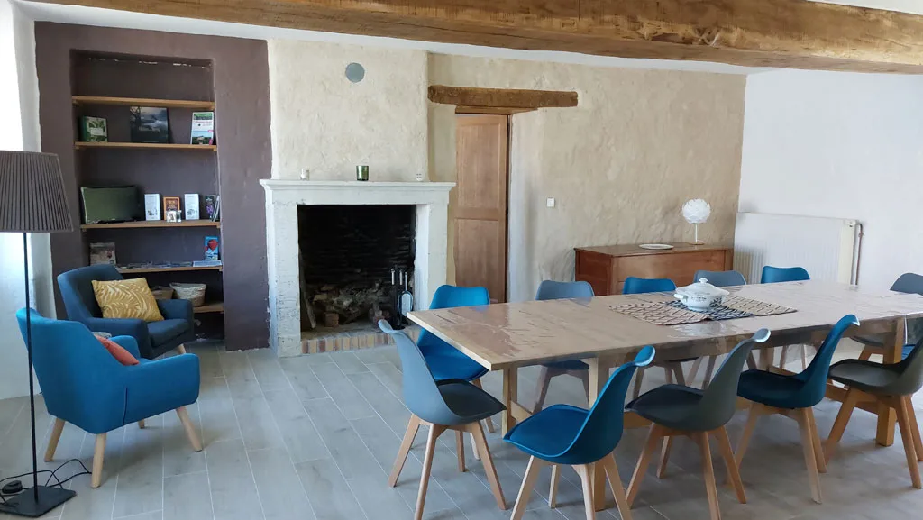 Salle à manger avec grande table en bois, cheminée en pierre et bibliothèque