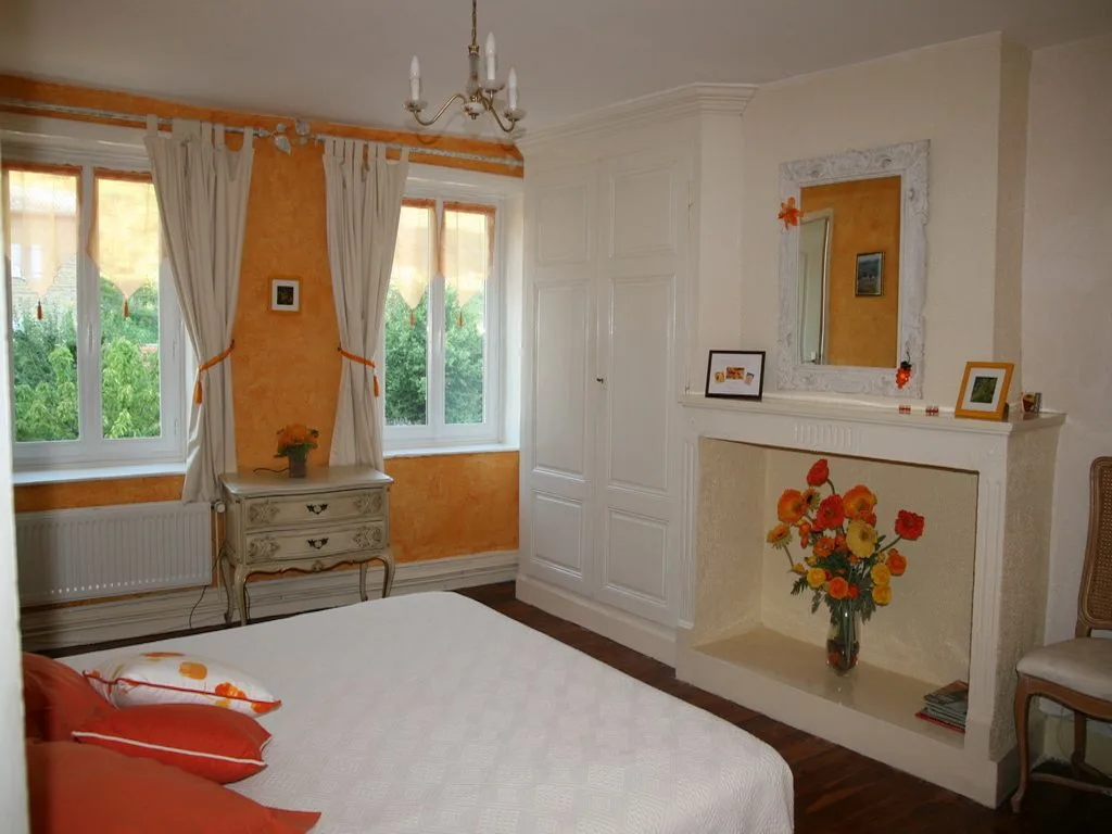 Chambre Ambre lumineuse avec cheminée, grand lit et fenêtres sur le village