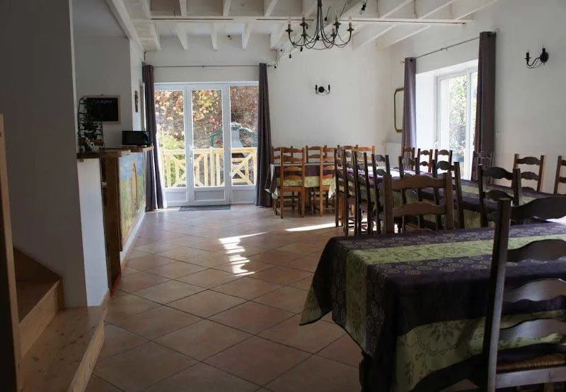 Grande salle à manger commune avec tables dressées pour un groupe et accès terrasse