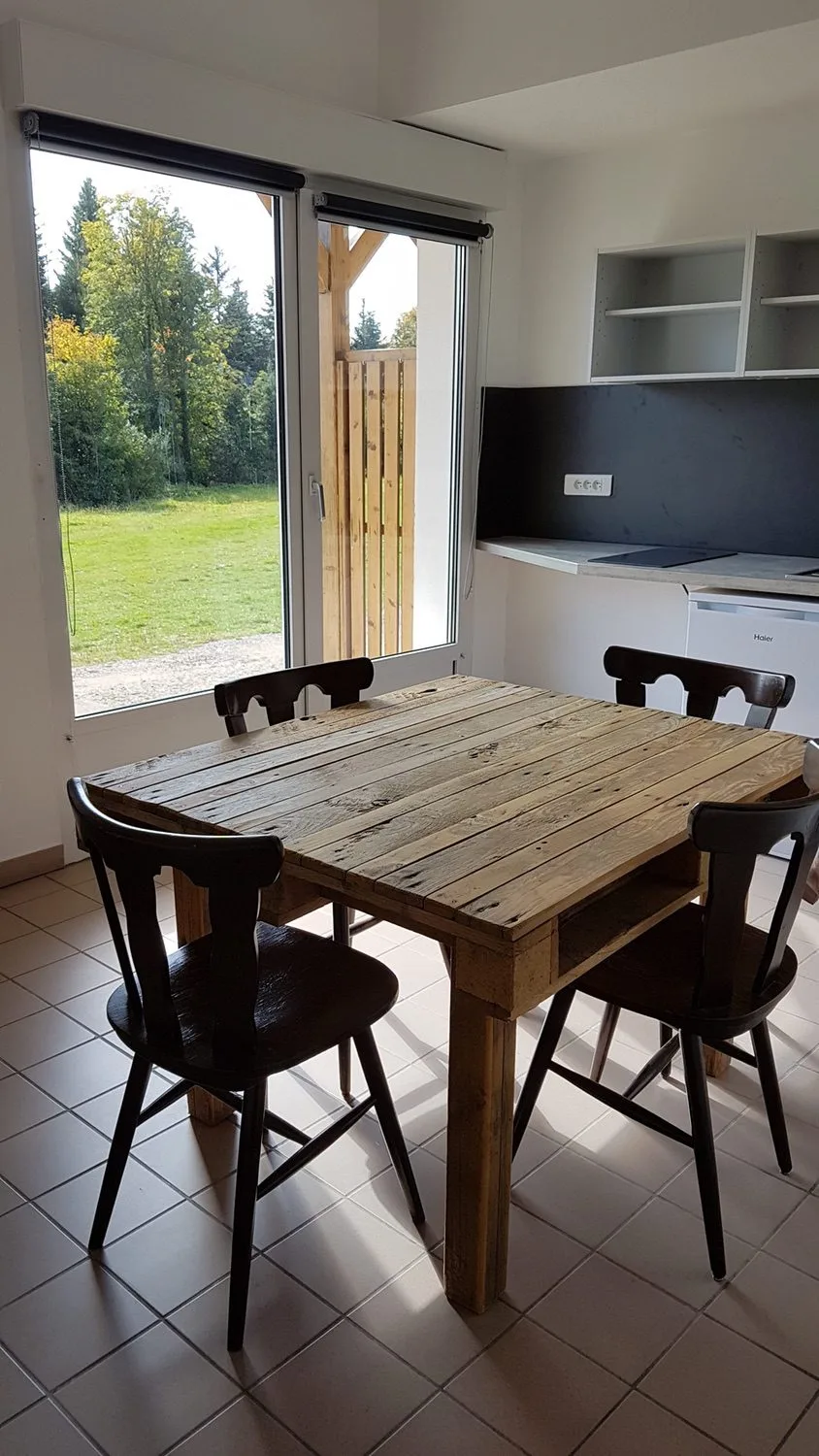 Cuisine équipée et table en bois brut avec chaises noires, baie vitrée sur l'extérieur