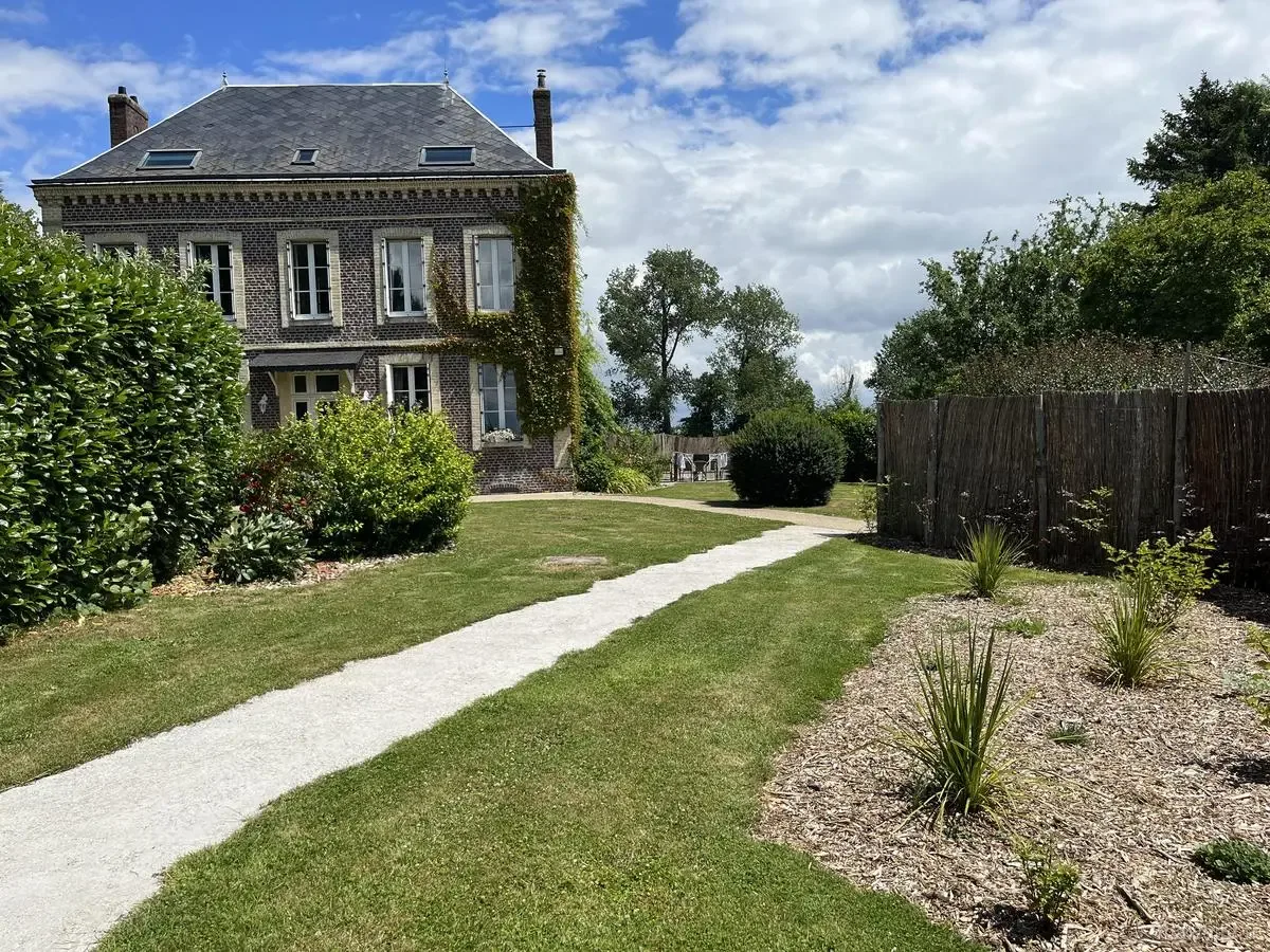 Allée de jardin menant à la façade arrière du gîte, entourée de pelouse et arbres