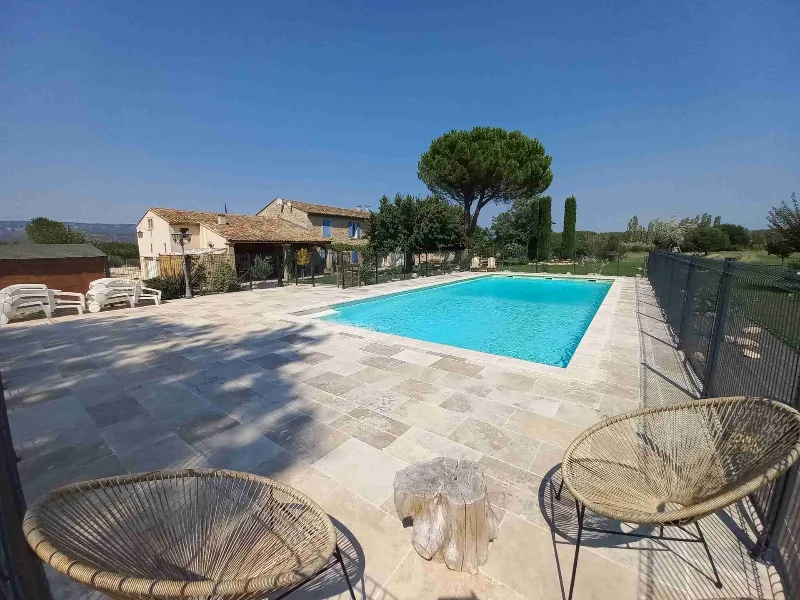 Vue d'ensemble du mas provençal en pierre avec piscine, terrasse en pierre et pinède au fond du jardin