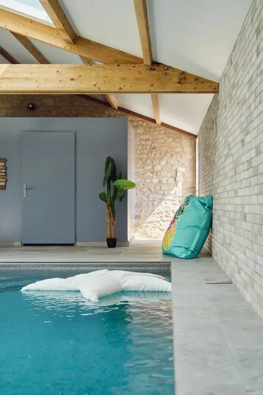 Piscine intérieure chauffée sous charpente en bois apparente avec mur en pierre du pays