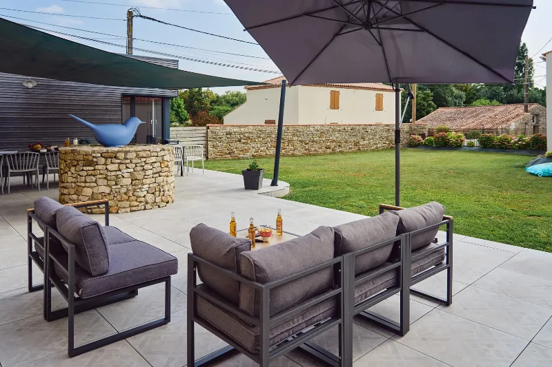 Terrasse extérieure avec salon de jardin, parasol et muret en pierre sèche donnant sur le jardin