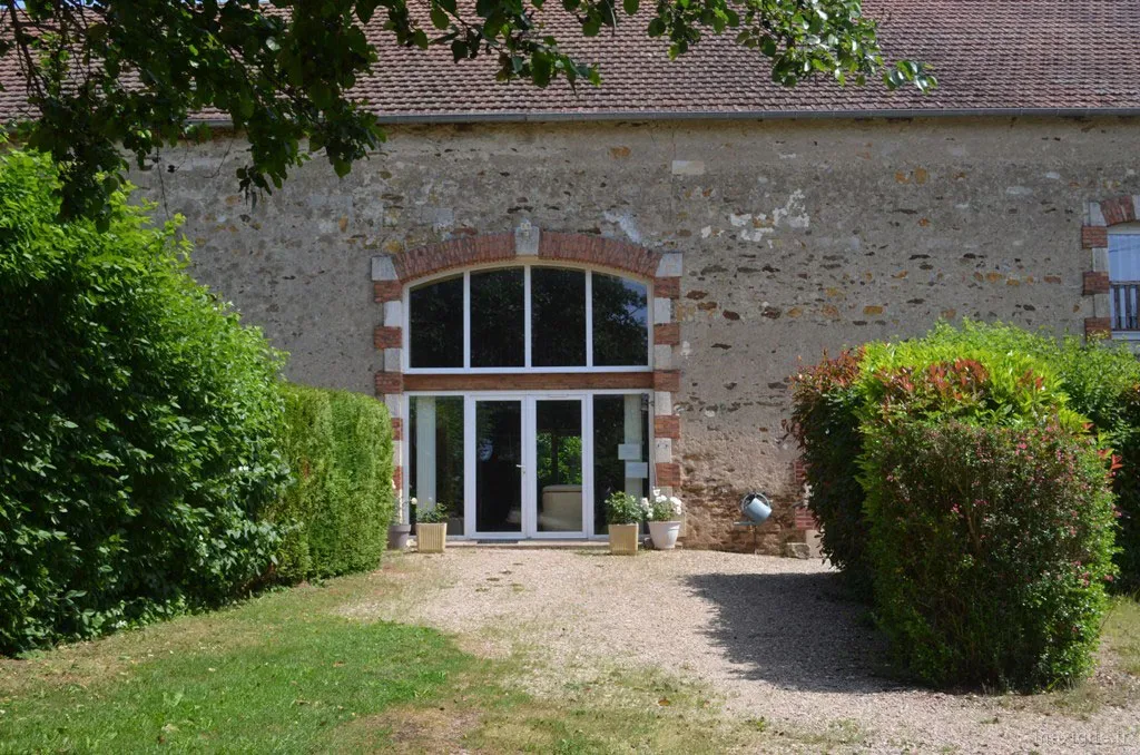 Entrée vitrée du gîte donnant sur un jardin arboré et fleuri