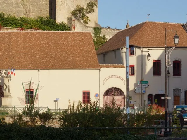 Façade en pierre du gîte au pied du château, entrée voûtée avec porte rouge