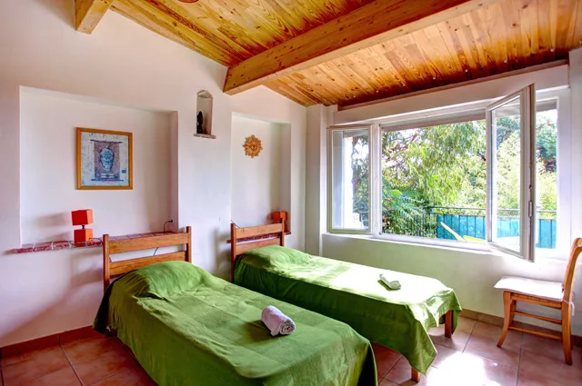 Chambre lumineuse à deux lits jumeaux avec charpente en bois et vue sur la verdure
