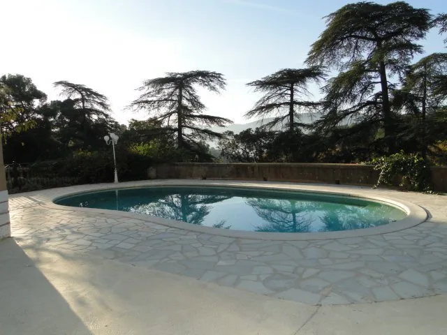 Façade de la bastide provençale avec porte-fenêtres vertes et arbres environnants