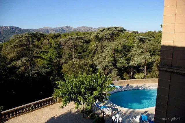 Vue plongeante sur la piscine et les collines boisées depuis la terrasse de la bastide