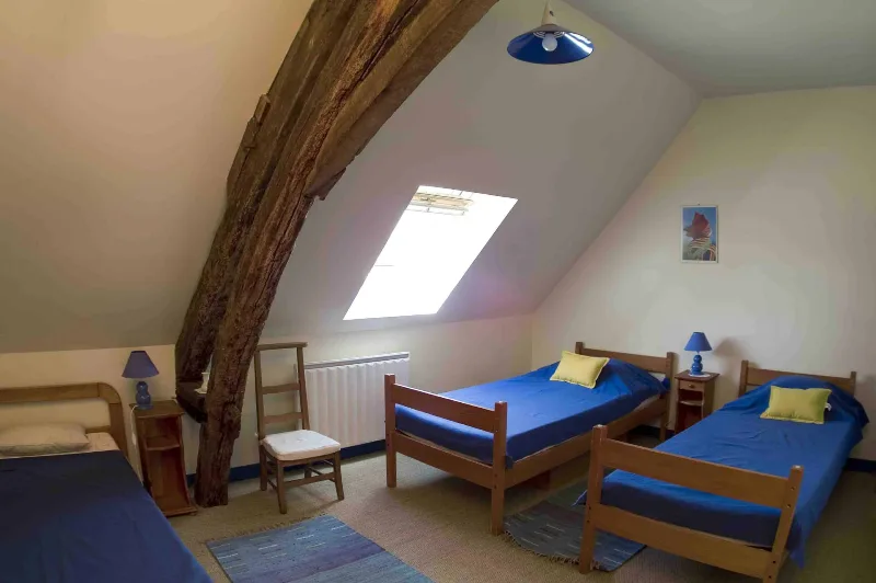Chambre avec lits simples aux parures bleues et poutre ancienne traversant la pièce