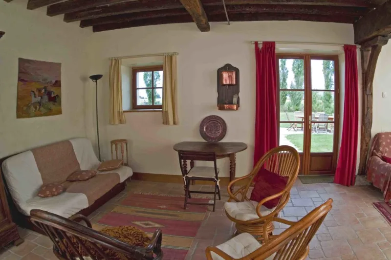 Salon avec canapés, fauteuils en osier et grande porte-fenêtre donnant sur la terrasse