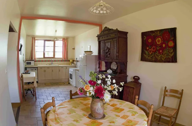 Cuisine équipée ouverte sur la salle à manger, avec buffet ancien et table ronde fleurie
