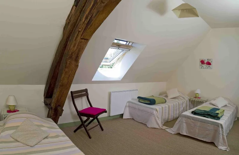 Chambre sous les combles avec plusieurs lits simples et charpente apparente
