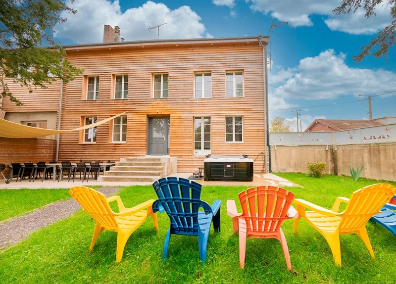 Jardin arboré avec spa extérieur, terrasse et chaises colorées derrière la maison