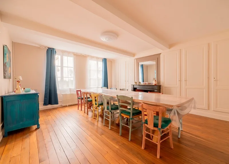 Grande salle à manger lumineuse avec longue table en bois et cheminée en marbre