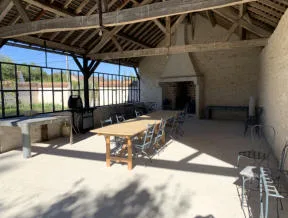 Halle extérieure couverte avec cheminée, grande table en bois et charpente apparente