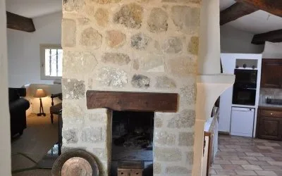 Grand salon avec cheminée en pierre, poutres apparentes et vue sur la cuisine