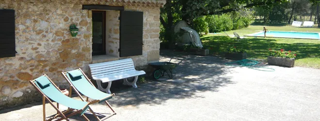 Terrasse avec transats et banc face à la façade en pierre, piscine en arrière-plan