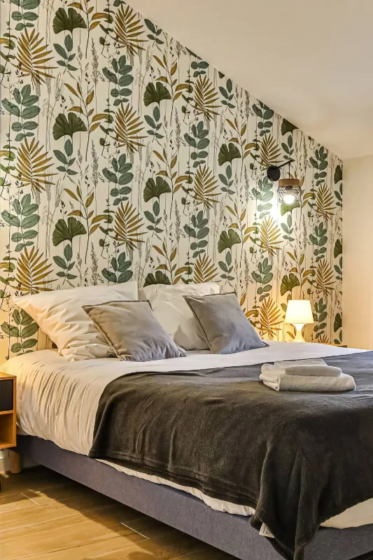 Chambre sous charpente avec papier peint feuillage et lit double