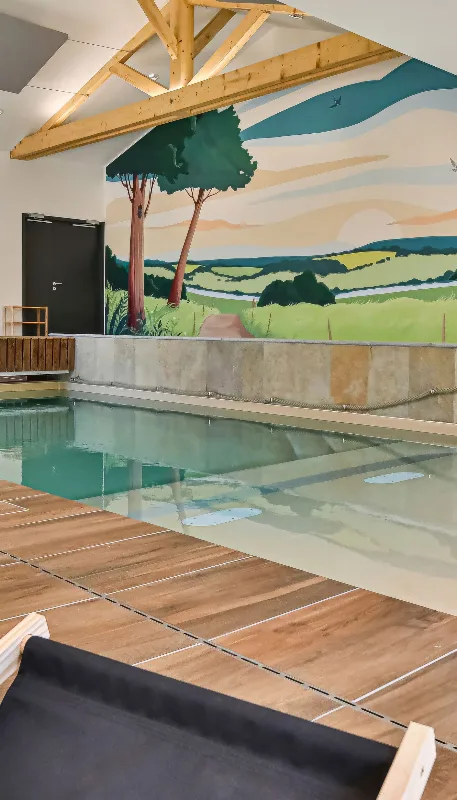 Piscine intérieure chauffée avec fresque murale champêtre et plage en bois