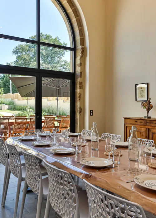 Grande salle à manger sous verrière avec longue table en bois pour les repas de groupe