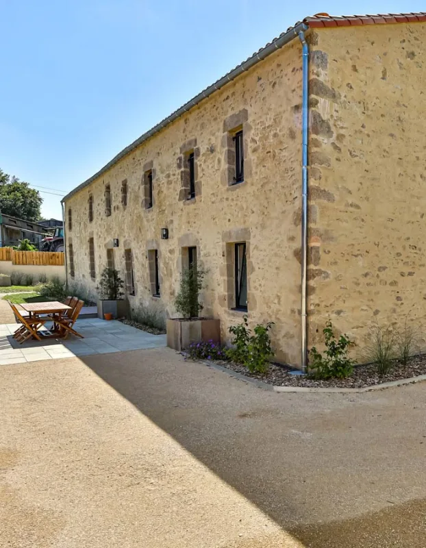 Façade en pierre de la longère avec toiture de tuiles et jardin fleuri