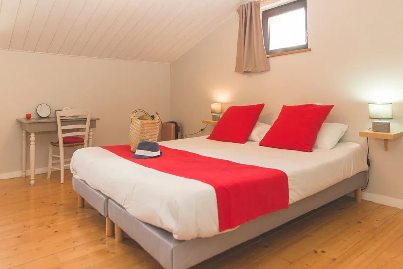 Chambre sous charpente avec lit double et coussins rouges