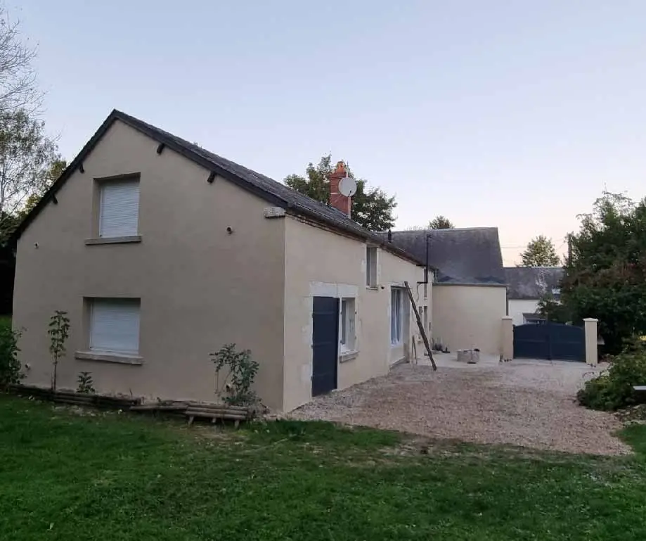 Façade de la Longère au crépi clair, portail et cour gravillonnée au crépuscule