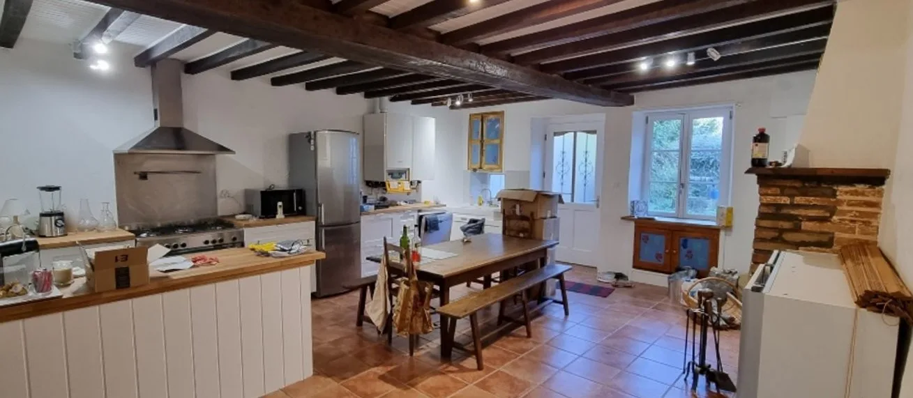 Cuisine équipée avec grande table en bois, four professionnel et poutres apparentes