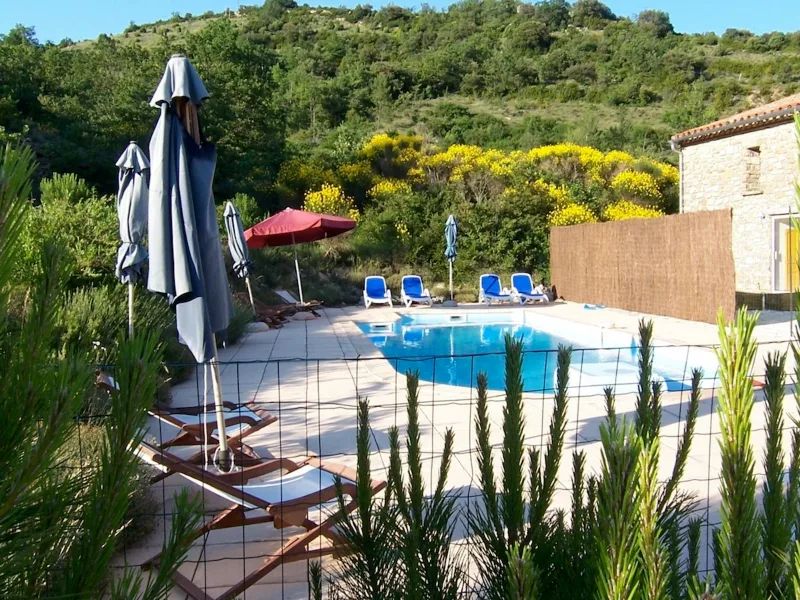 Les Gîtes du Torgan – MassacPiscine entourée de transats et parasols, au coeur de la garrigue avec bâtiment en pierre