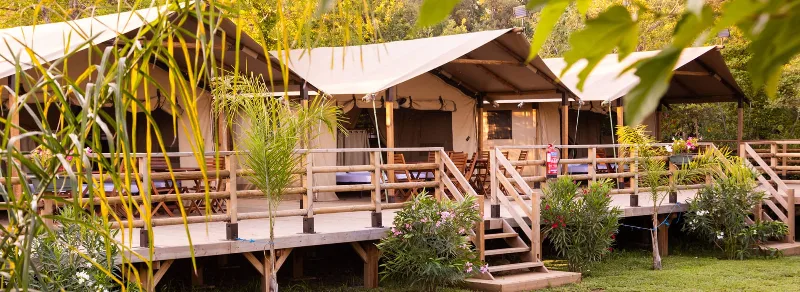 Rangée de lodges tentes en bois sur pilotis, entourés de végétation méditerranéenne