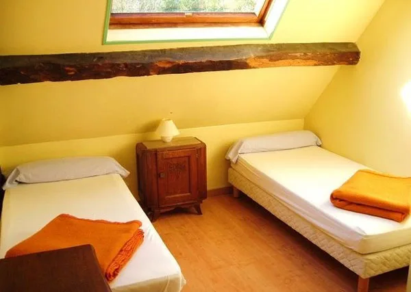 Chambre lumineuse avec deux lits simples séparés par une table de chevet, sous poutre en bois