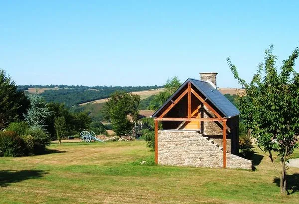 Bâtiment annexe en pierre avec charpente apparente, entouré d'un grand terrain arboré