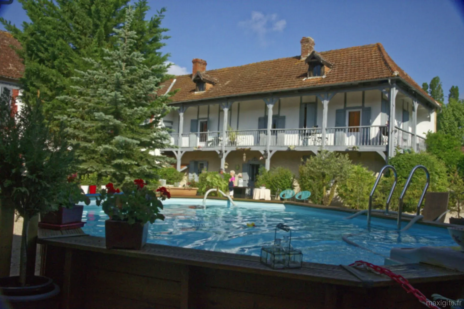 Gîte de groupe Domaine des Mousquetaires à Laas — Vue de la maison de maître depuis la piscine entourée d'un jardin fleuri, capacité 25 personnes