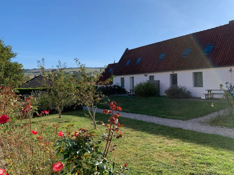 Façade en pierre du gîte avec jardin verdoyant et ciel dégagé au-dessus des toits