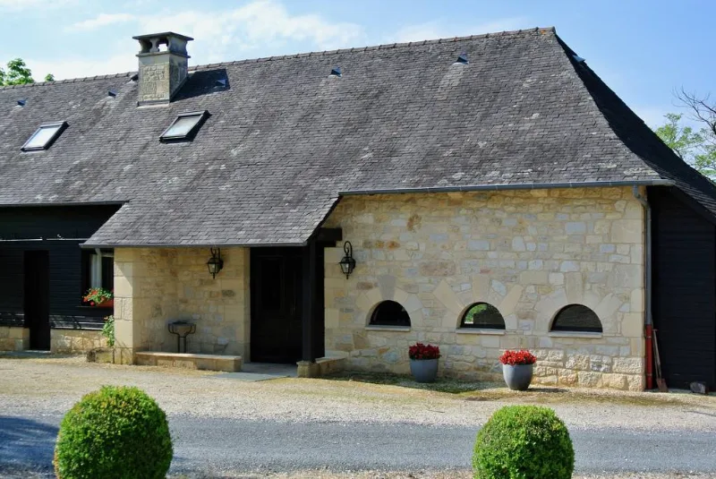 Façade en pierre de l'un des gîtes avec ses volets bruns et sa terrasse fleurie