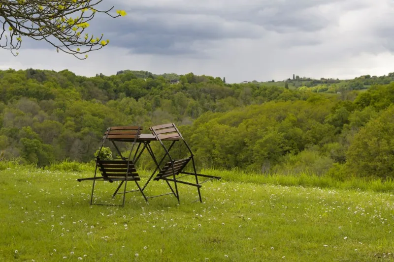 Table et chaises pliantes installées dans la prairie avec vue panoramique sur la vallée boisée