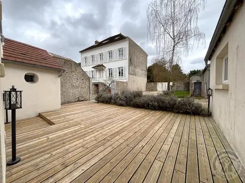 Terrasse en bois donnant sur la façade arrière de la maison, entourée de gravier et de végétation