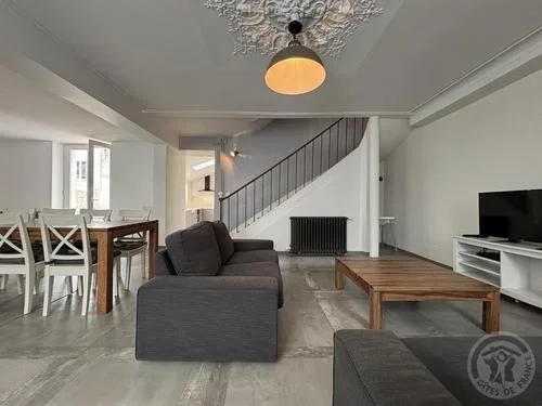 Salon confortable avec canapés gris, table basse en bois et escalier menant à l'étage