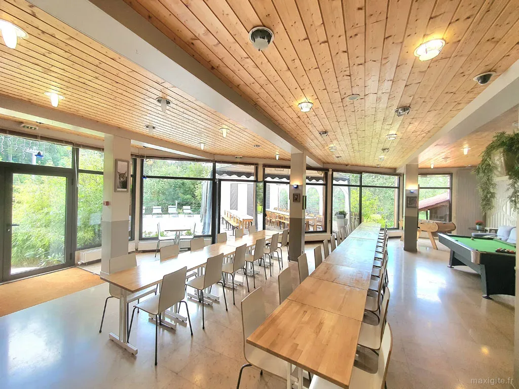 Grande salle à manger commune avec charpente en bois et longues tables pour les repas de groupe