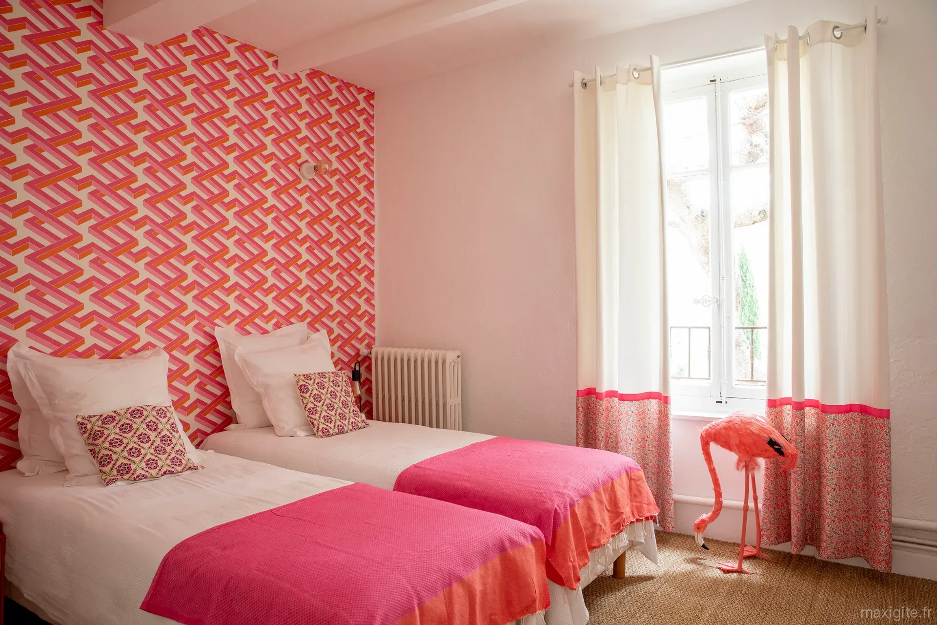 Chambre double lumineuse avec deux lits, papier peint graphique rose et fenêtre sur le domaine