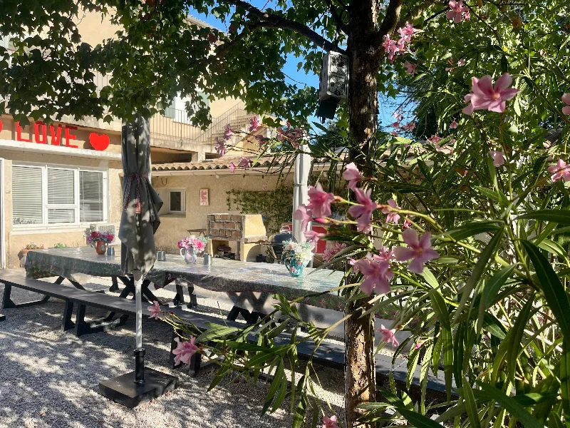 Terrasse ombragée avec grande tablée conviviale, guirlande lumineuse et barbecue en pierre