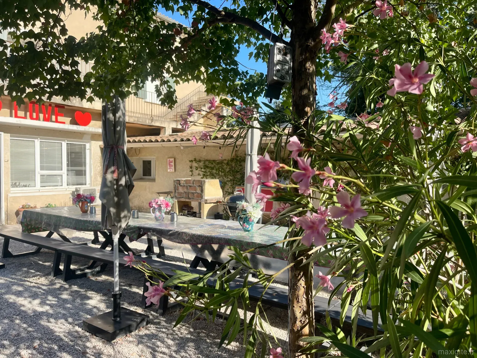 Terrasse ombragée avec grande tablée conviviale, guirlande lumineuse et barbecue en pierre