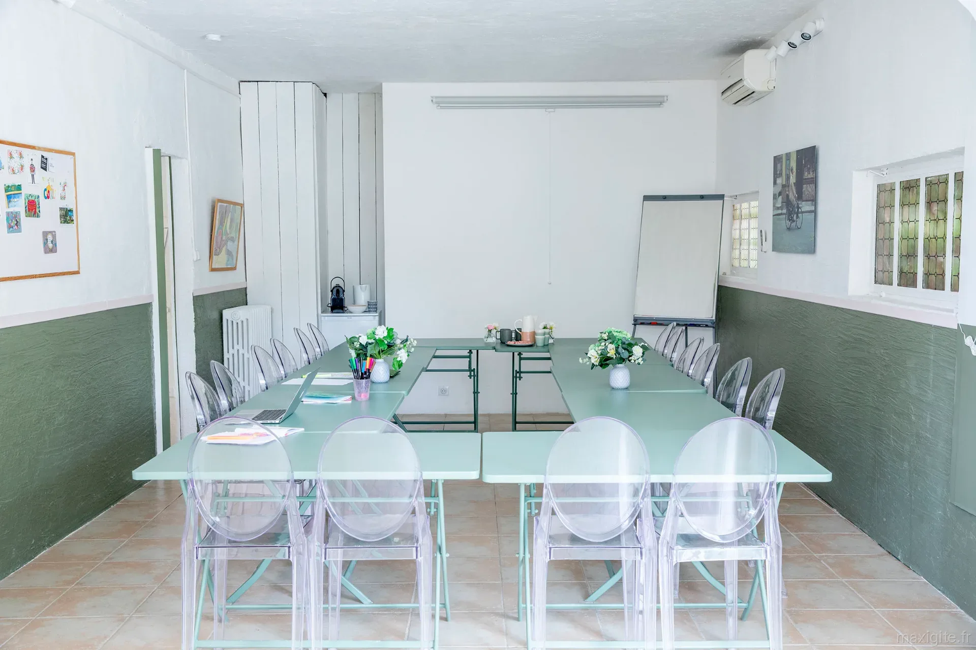 Salle de réunion aménagée avec grande table modulable, chaises transparentes et tableau paperboard